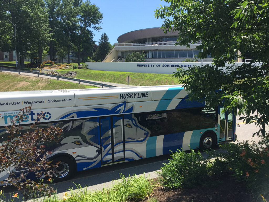 Bus with "Husky Line" on the side parked near the University of Southern Maine. The bus features a graphic of a husky.